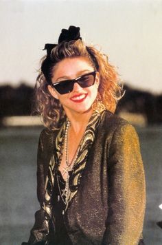 a woman wearing sunglasses and a black top with a bow in it's hair