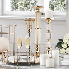 a table topped with candles and glasses filled with champagne next to white roses in front of a window