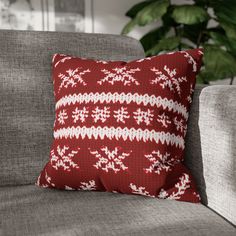 a red and white christmas pillow sitting on top of a gray couch next to a potted plant