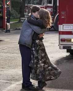 a man and woman embracing in front of a fire truck with their arms around each other