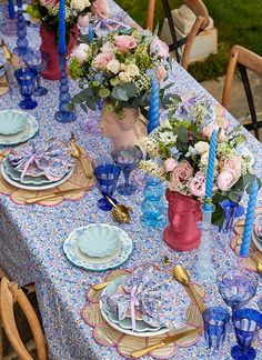 the table is set with blue and pink dishes, candles, and flowers in vases