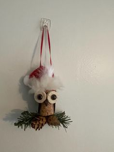 an owl ornament hanging on the wall with pine cones and red ribbon around its eyes