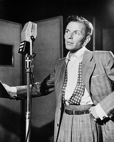 a man in a suit and tie standing next to a microphone with one hand on his hip