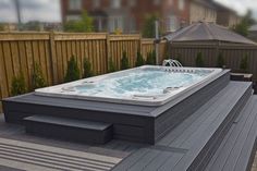 a hot tub sitting on top of a wooden deck next to a fenced in area