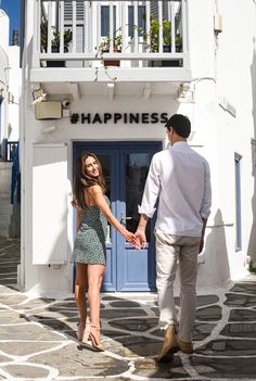 a man and woman holding hands in front of a building with the words happiness written on it