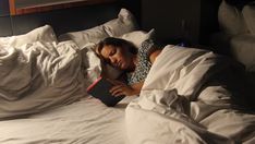 a woman is laying in bed with her head on the pillow and reading a book