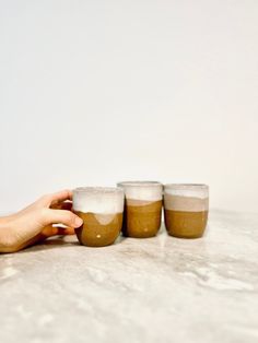 three cups are sitting on the table with one hand reaching for it