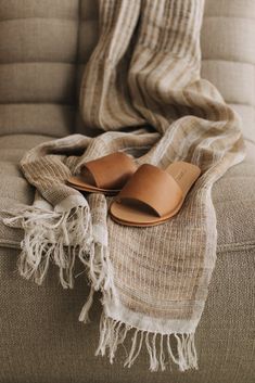 a pair of brown sandals sitting on top of a couch next to a throw blanket