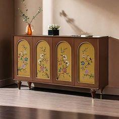 a sideboard with flowers painted on it in the corner of a room next to a window