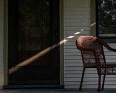 a wicker chair sitting in front of a door on the side of a house