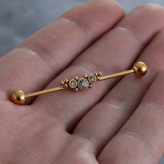 a hand holding a gold nose pin with two balls on it's end and one bead in the middle