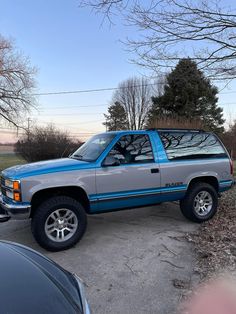 a silver and blue truck parked in a parking lot next to some trees with no leaves on them