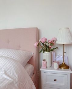 a bed with pink flowers in a vase on top of it next to a night stand