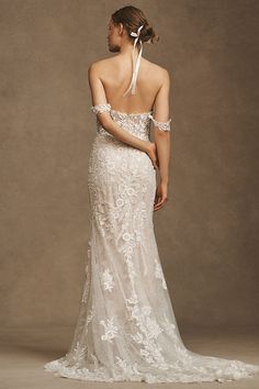 a woman in a wedding dress with an open back and white flowers on the shoulder