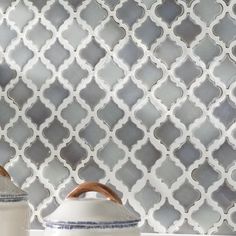 two white vases sitting on top of a counter next to a wall with grey and white tiles