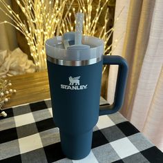 a stainless steel travel mug sitting on top of a checkered tablecloth with the word stanley written on it