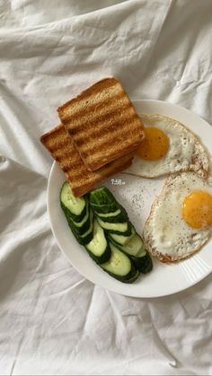 an egg, cucumber and toast are on a plate with white linens