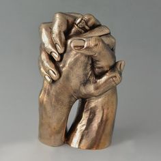 a gold colored sculpture of two hands holding each other's fingers with one hand on top of the other