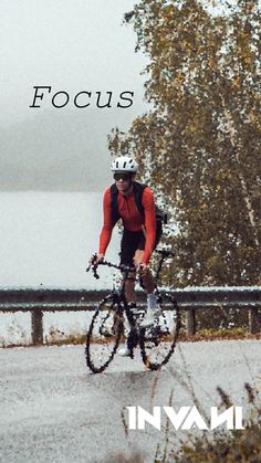 a man riding a bike down a road next to a lake with trees in the background