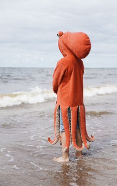 an orange octopus stuffed animal standing in the water at the beach with its head sticking out