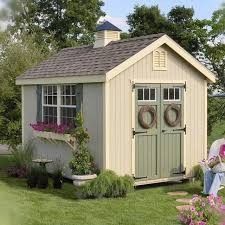 a garden shed with flowers and wreaths on the door, next to a bench