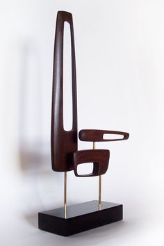 a wooden sculpture sitting on top of a black stand next to a white wall and floor