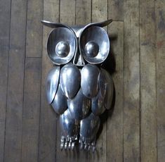 an owl made out of metal spoons sitting on top of a wooden floor next to a wall