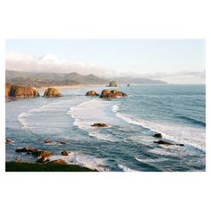 an aerial view of the ocean with rocks in the foreground and mountains in the background