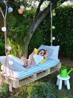 a woman is laying in a swing bed with pillows on it and a green watering can next to her