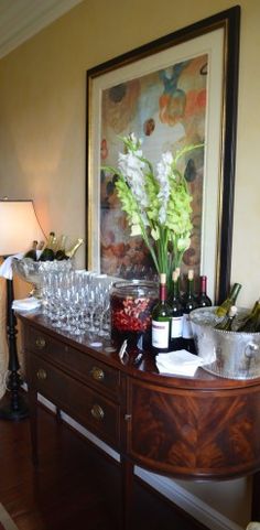 a table with wine glasses and bottles on it in front of a framed art piece