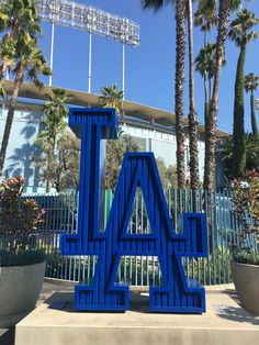 the los angeles dodgers logo is painted blue in front of palm trees and a fence