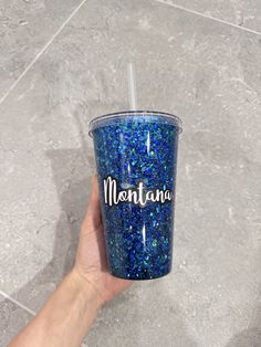 a hand holding a blue glittered cup with the word montana written on it in white lettering