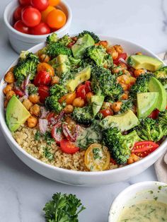 a white bowl filled with broccoli and quinoa salad next to a bowl of tomatoes