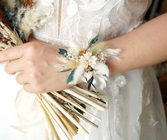 a woman in a white dress holding a bouquet of feathers and flowers on her arm