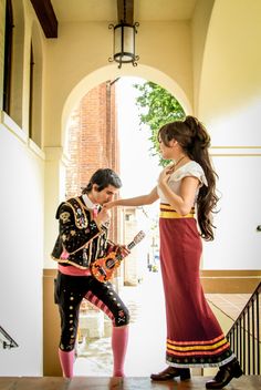 two women dressed in costumes playing guitars on the steps to an open door with a brick wall and arched doorway behind them