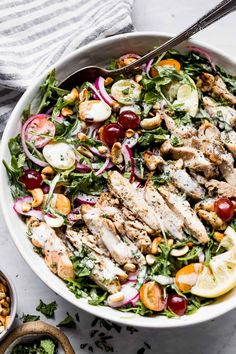 a white bowl filled with chicken, salad and dressing on top of a marble table