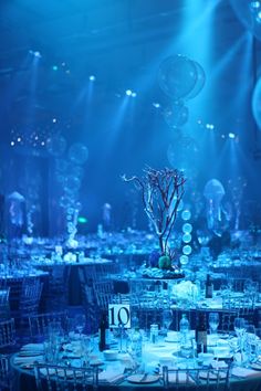 the tables are set for an event with blue lighting and balloons in the air above them