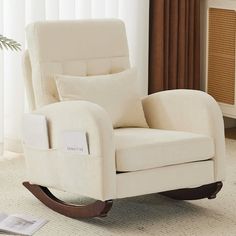 a white rocking chair sitting on top of a rug in a living room next to a window