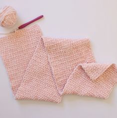 a pink knitted blanket next to a ball of yarn and a crochet hook