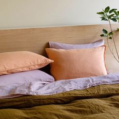 a bed topped with pillows and blankets next to a plant on top of a wooden headboard