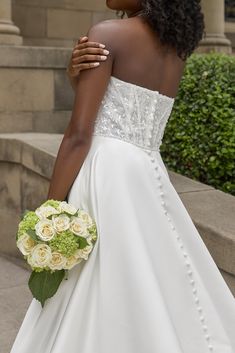 a woman in a white wedding dress holding a bouquet of flowers and looking off into the distance