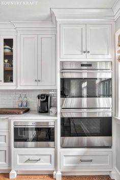 a kitchen with white cabinets and stainless steel ovens in the center, along with wooden flooring