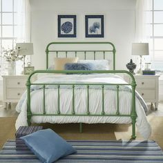 a green metal bed in a white bedroom with blue pillows and pictures on the wall