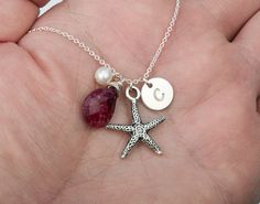 "This beach-themed starfish initial birthstone necklace features: 1. one sterling silver starfish charm (smooth or textured (shown in picture)) 2. a disc charm (22ga, 3/8\") stamped with an initial in your choice of font (14 available) 3. a custom birthstone of your choice 4. one small freshwater pearl 5. a sterling silver chain (several lengths available) closed with a lobster clasp. You can expect the highest stamping quality from my shop - thick gauge discs, uniformly deep impression, perfect Starfish Charms Jewelry For Gifts, Starfish Charms Jewelry For Gift, Ocean-inspired Starfish Charm Necklace For Gift, Starfish Charms Jewelry As Gift, Starfish Charms Jewelry As A Gift, Personalized Ocean-inspired Jewelry Gift, Ocean-inspired Starfish Charm Necklace Gift, Starfish Charm Necklace Perfect For Gifts, Starfish Charm Necklace As Gift