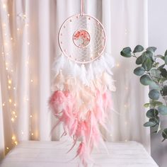 a pink and white dream catcher sitting on top of a table next to a potted plant