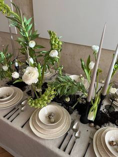 the table is set with plates and silverware, flowers and greenery in vases