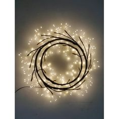 a lighted wreath with white lights in the center and branches around it on a wall