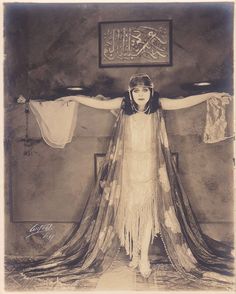 an old fashion photo of a woman standing in front of a bed with her hands on her head