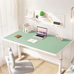 a laptop computer sitting on top of a green desk next to a white chair in front of a window