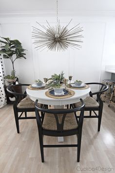 a dining room table with chairs and plates on it, surrounded by potted plants